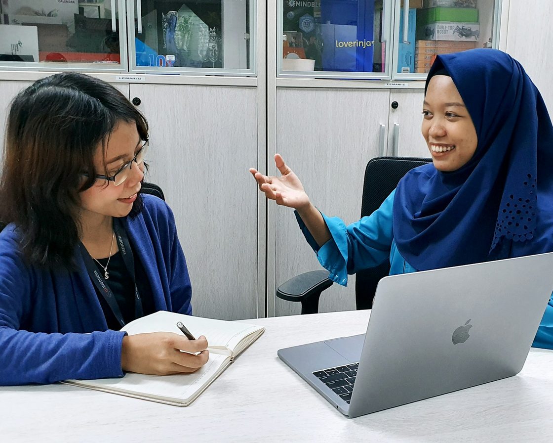 Dua perempuan berdiskusi di depan laptop di kantor sambil memeriksa NPWP