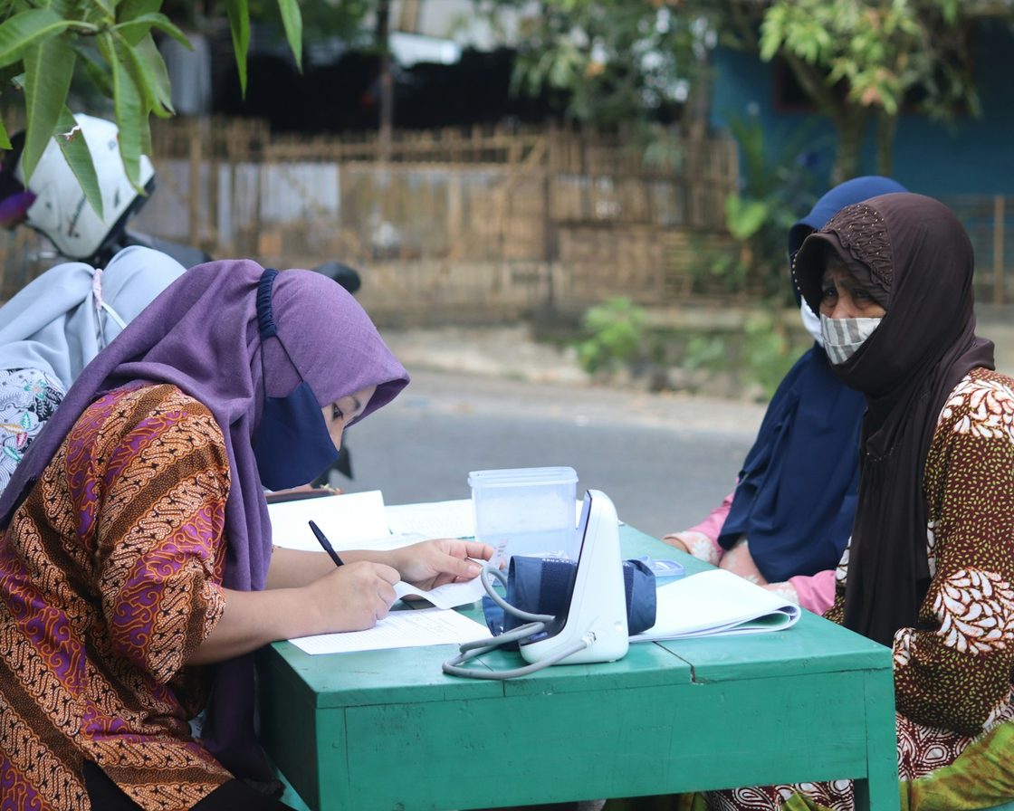 Dua perempuan berhijab mengurus berkas di meja pelayanan, membereskan keterlambatan lapor
