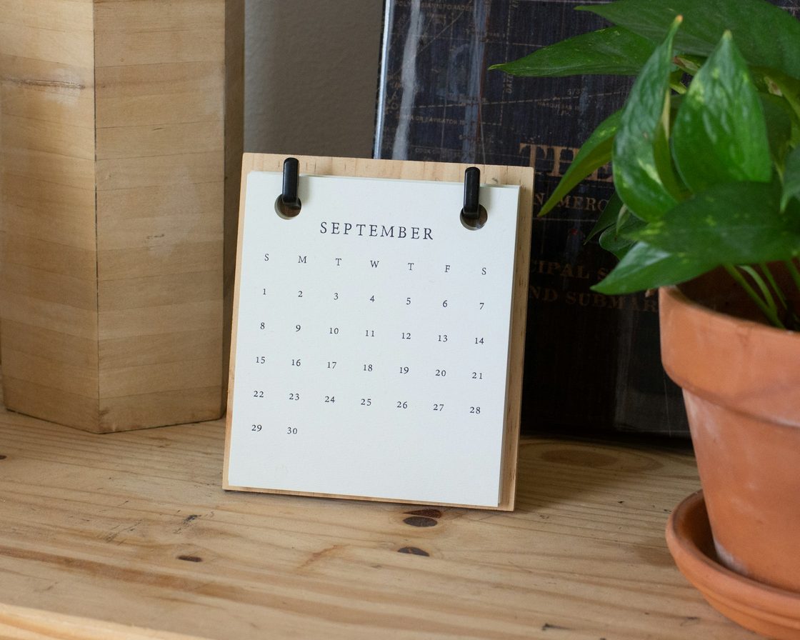 Kalender meja bulan September di meja kayu di samping tanaman