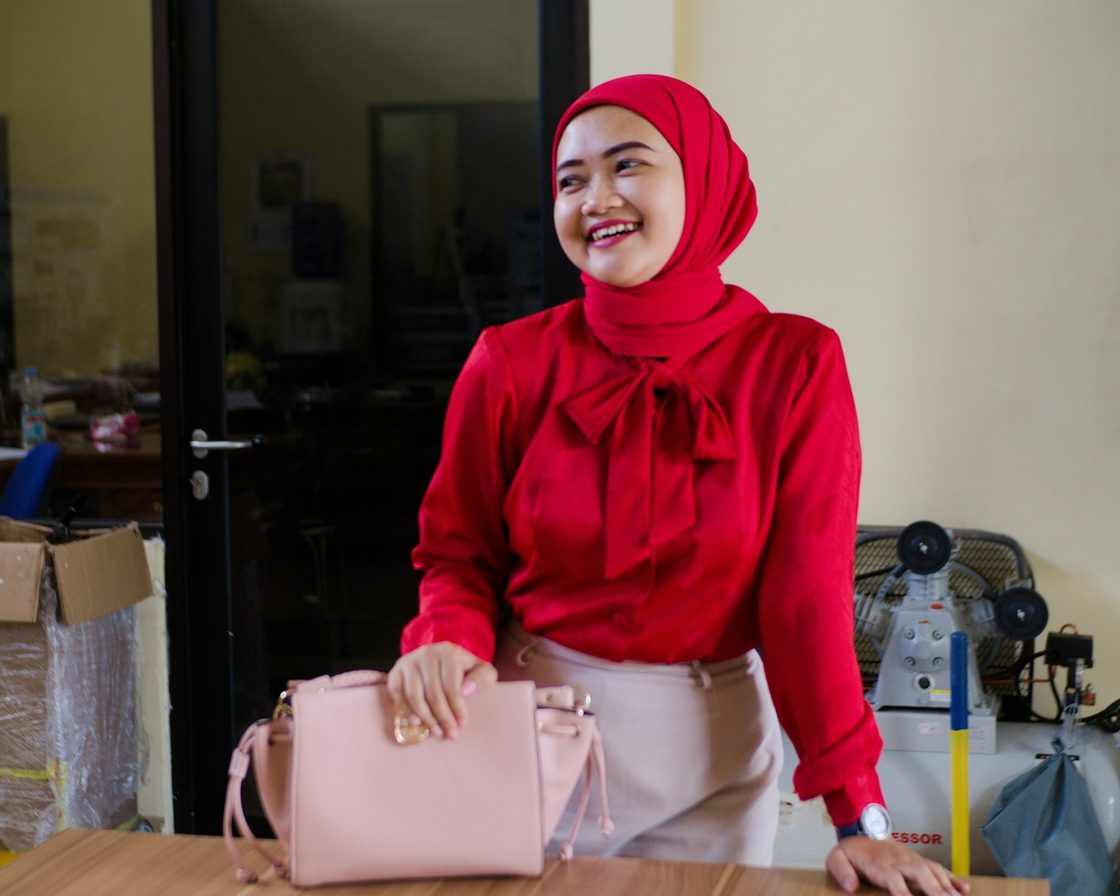 Karyawan berhijab merah tersenyum di ruang kantor, gambaran penerima gaji yang dipotong PPh 21