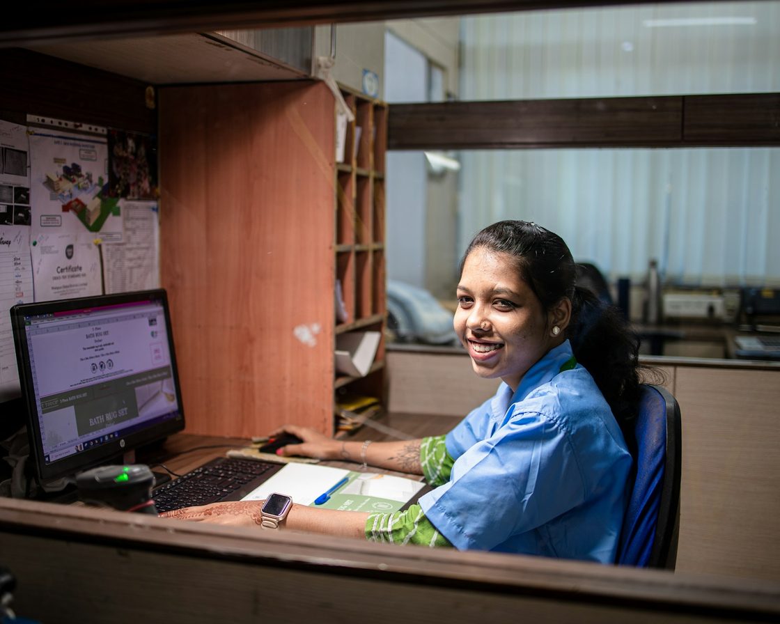 Perempuan tersenyum di meja kerja kantor dengan komputer, siap menjawab pertanyaan