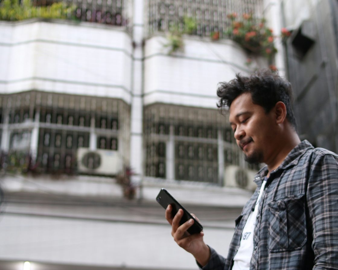 Pria memeriksa ponsel di depan ruko, bersiap mengaktivasi akun Coretax
