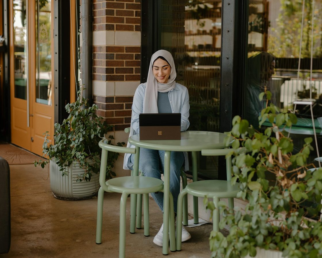 Perempuan berhijab mendaftar akun lewat laptop di teras kafe