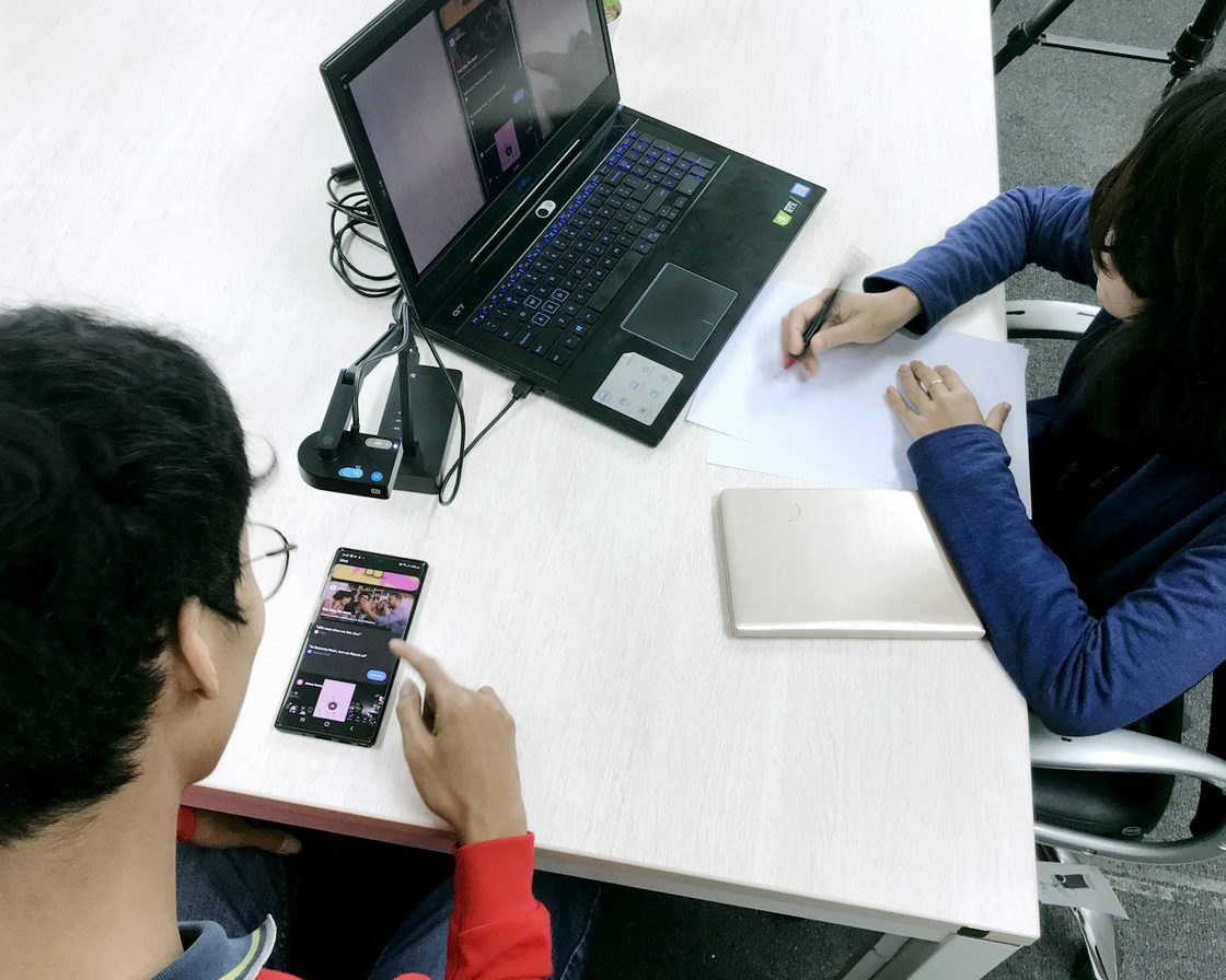 Dua orang di meja kerja, satu memegang ponsel dan satu di laptop, mengurus EFIN