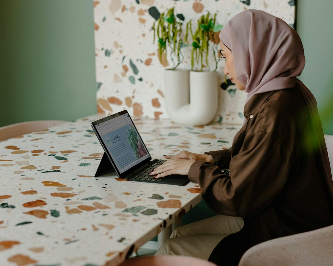 Perempuan berhijab mengetik di laptop, mengisi SPT Tahunan di Coretax