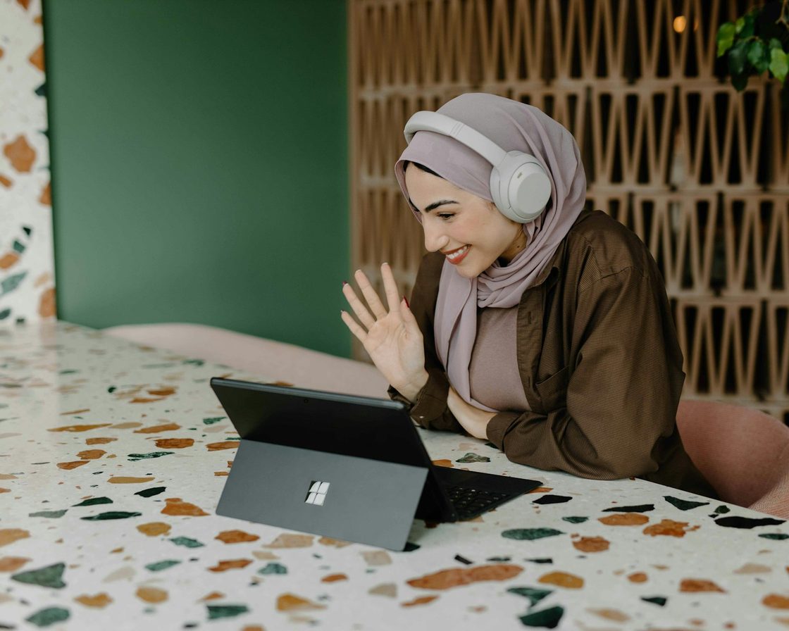Perempuan berhijab dengan headphone menghadap laptop saat lapor SPT Tahunan