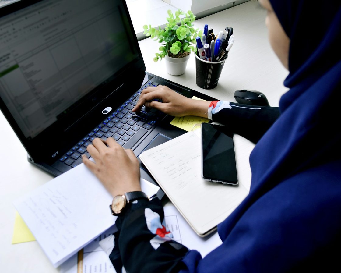 Tangan mengetik di laptop di meja kerja, menghitung THR dan bonus