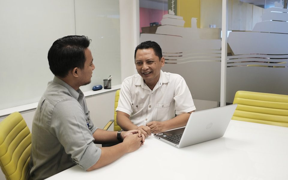 Dua pria Indonesia berdiskusi serius dengan laptop tentang surat dari kantor pajak